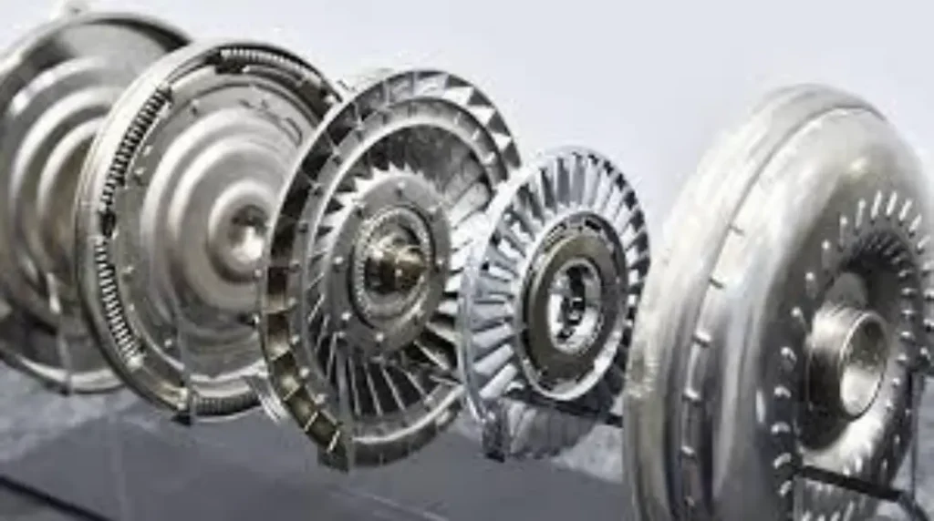 A series of disassembled torque converter components lined up, showing the various metal parts and fins.