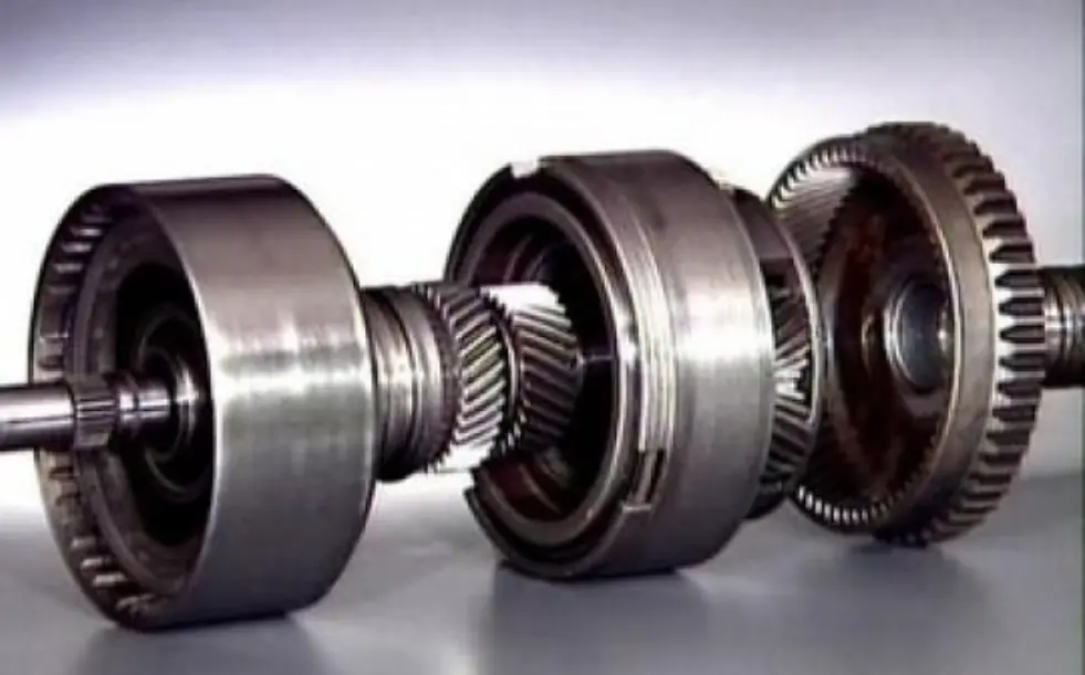 Disassembled components of a planetary gear set, featuring a central gear, surrounding gears, and an outer ring gear on a shaft.