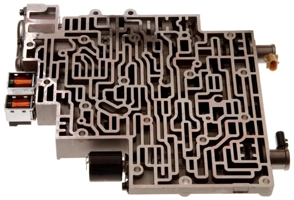 A detailed view of a transmission valve body, showing a complex maze of passages, valves, and solenoids.
