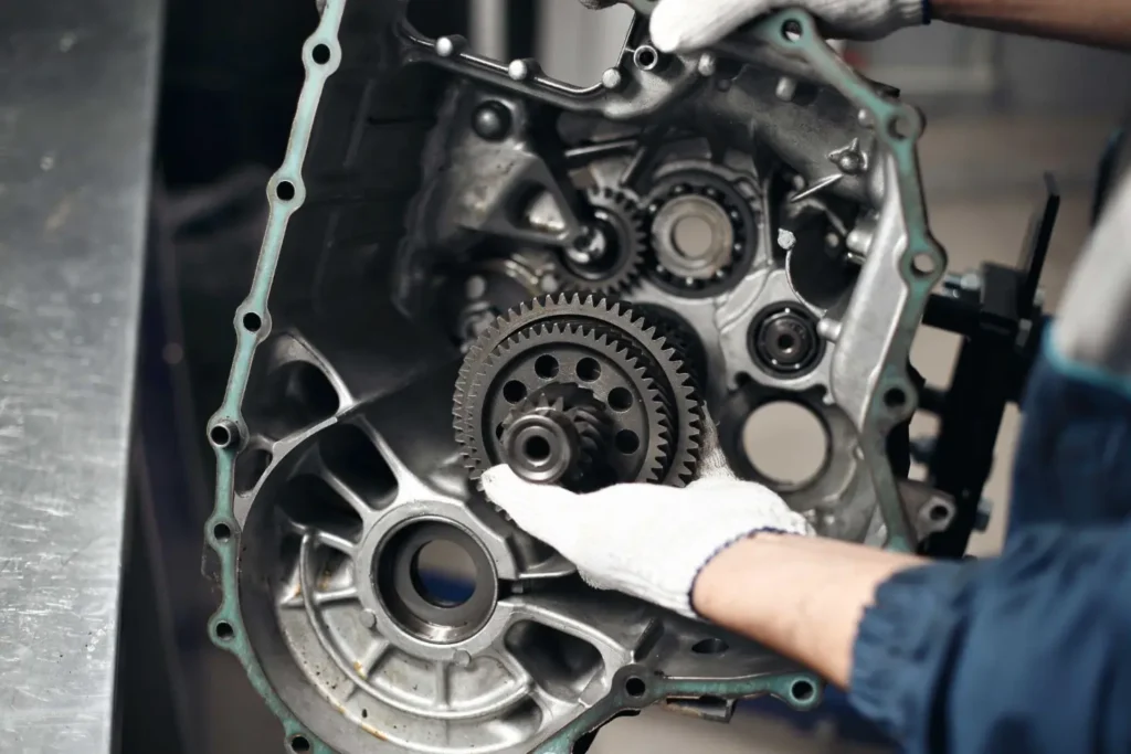 A close-up of an automatic transmission's internal components, including gears and shafts, being worked on by a mechanic's hands.