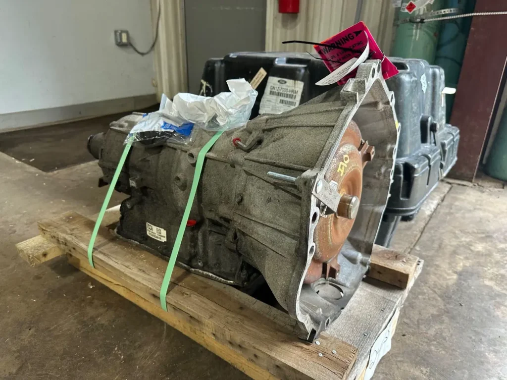 A used automatic transmission unit securely strapped to a wooden pallet, ready for transport or storage.