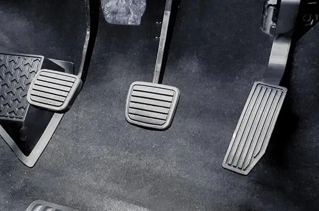 A view of three pedals on the floor of a car: clutch (left), brake (middle), and accelerator (right).